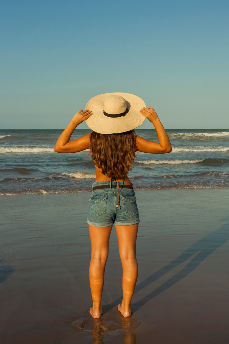 Young woman from behind, wearing beach summer hat